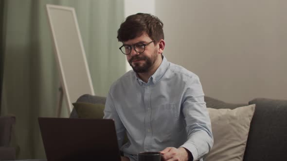 A Serious Man Works on a Laptop and Drinks Coffee