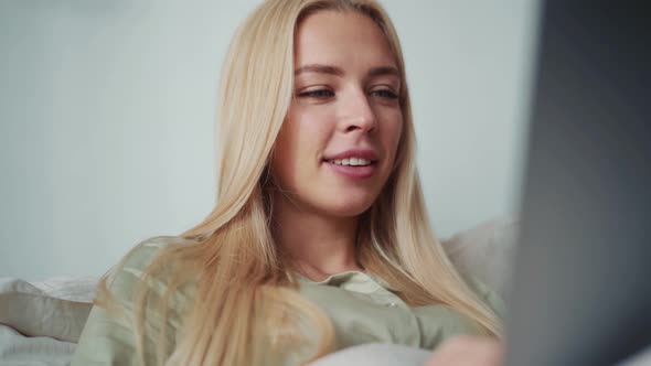 Positive blond woman working on laptop in bed