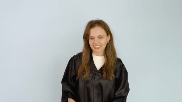 Young Caucasian Female Student in a Black Robe Lightly Throws a Square Hat with a Tassel Up and