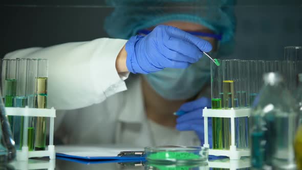 Left-Handed Researcher Adding Green Powder to Tube and Making Notes, Experiment