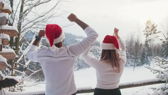 Happy Young Couple with Christmas Hats Enjoying Snowfall on the Mountain