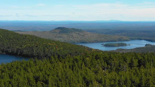 Aerial drone shot flying over a forested ridge to reveal blue mountain lakes in the forest along a m