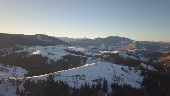 Aerial view of small village with scattered houses on snow covered hills in winter and bare dark