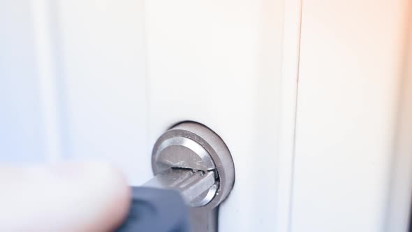 Pulling a Perforated Key From the Lock Cylinder of a White Plastic Door Closeup in Slow Motion