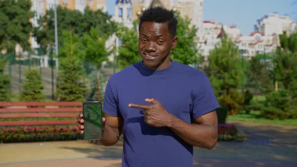 Smiling AfroAmerican Man Finger Points Smartphone Display with Green Screen