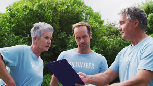 Caucasian senior couple with clipboard and man wearing volunteer t shirts talking in field