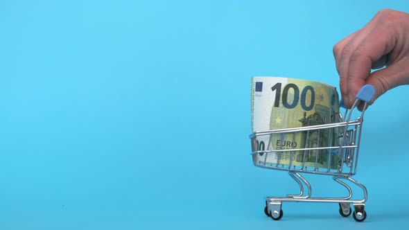 Shopping Cart with One Hundred Euro Banknote on Blue Background Buying Currency