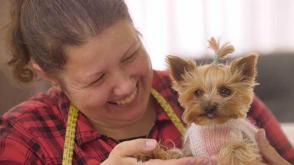 Smiling Woman Holding Cute Puppy Dressed in Pink Sweater