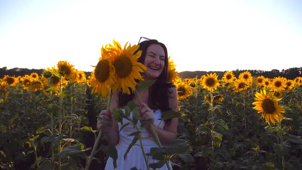 Young Smiling Woman Playing with Sunflower at the Field Under Blue Sky at Sunset. Funny Girl Hiding