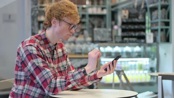 Attractive Young Redhead Man Using Smartphone in Cafe 