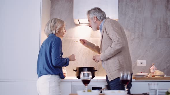 Slow motion shot of mature couple with red wine cooking in kitchen