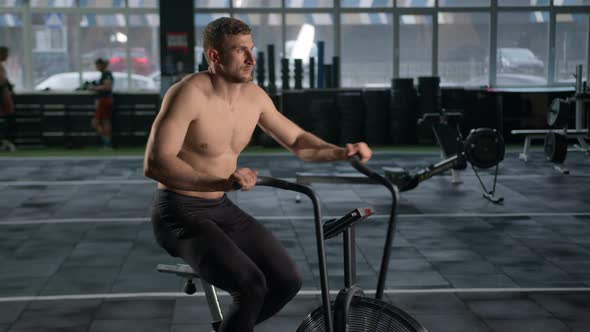 Young male athlete trains cardio on bike with fan, cardio and endurance training