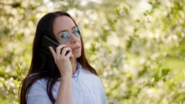 Adult Positive Woman is Talking By Cellphone in Blooming Garden Portarit of Pretty Lady in Spring