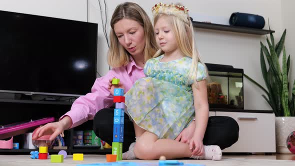 mother or nanny playing with child and building from colorful blocks cubes, having fun.