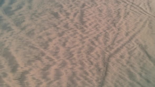 Revealing drone shot of incoming waves on a long beach with dunes on the rigth side