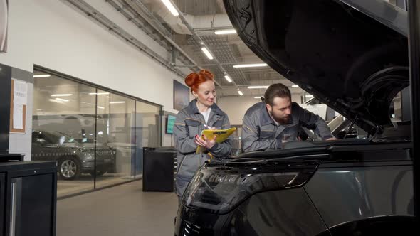 Two Professional Car Mechanics Examining Engine of a Car, Making Notes