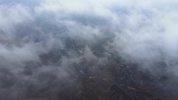Aerial View From High Altitude of Distant City Covered with Puffy Cumulus Clouds Flying By Before