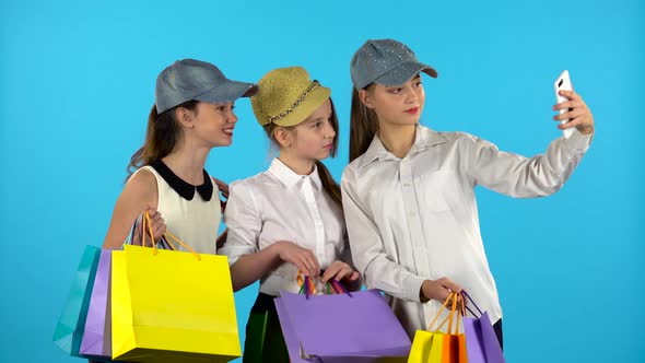 Three Teenagers Make Selfies with Colorful Packages. Blue Background