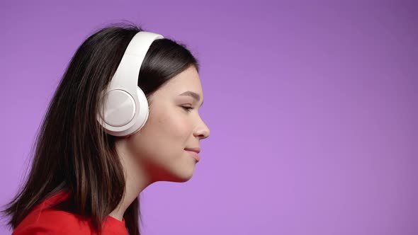 Young Woman Listening To Music Dancing with Headphones on Violet Studio Background