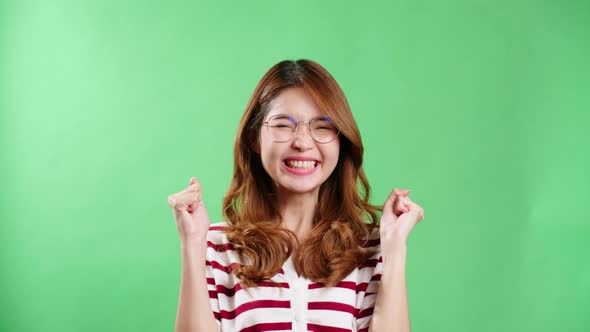 Cheerful young Asian woman with eyeglasses raising hands up, shaking and having fist pump from happi