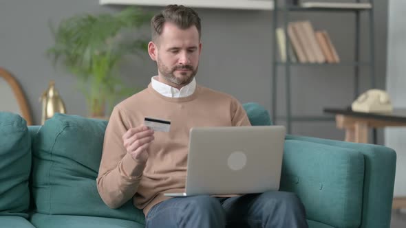 Man Making Online Payment on Laptop on Sofa