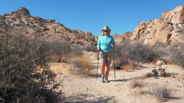 Mature Woman Walking In Dry Sandy Hot Desert With Huge Rocks Hills Bushes Cacti