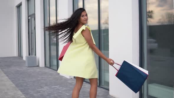 Beautiful Girl Model in a Long Dress After Shopping with Colored Bags in Hands Having a Good Mood