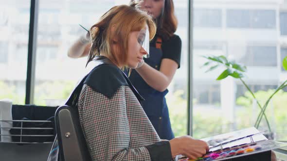 Professional woman hairstylist dyeing young woman customer's hair or change color in beauty salon.