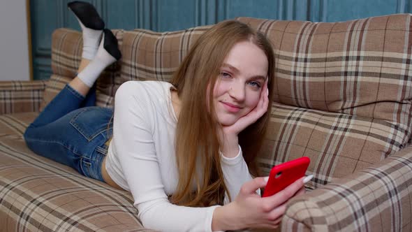 Girl Looks at Screen of Mobile Smartphone Makes Successful Online Order Smiles and Looks at Camera