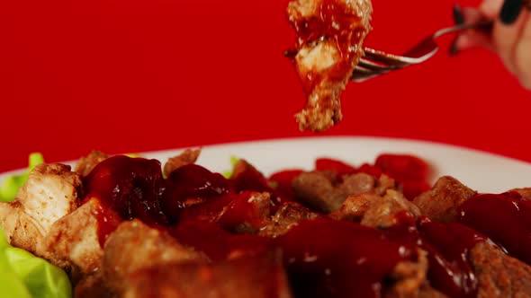 A woman's hand with a fork dips a piece of meat in ketchup on a red background.