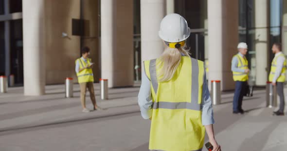 Back View of Female Engineer in Safety Hardhat and Vest Entering Office Building