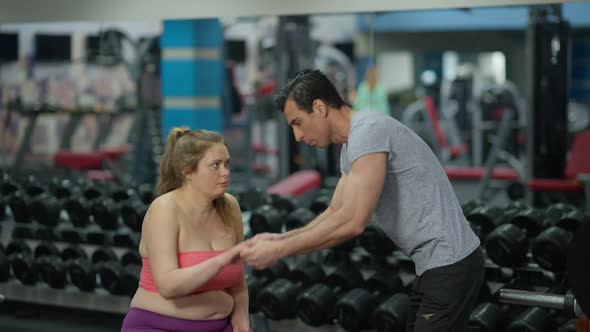 Overweight Caucasian Woman Sitting on Exercise Bench As Fit Middle Eastern Man Talking Explaining