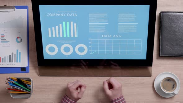 Shot From Above of a Man Looking at a Monitor with Company Data Graphs