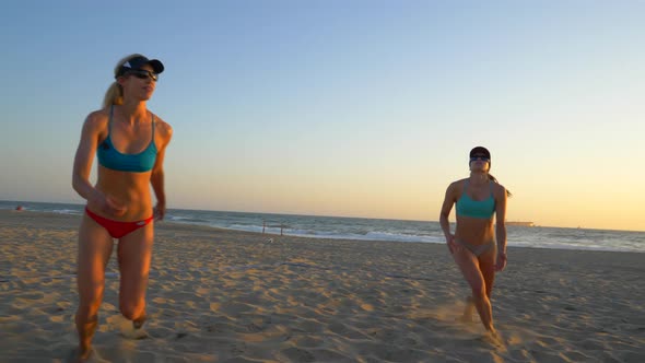 Women players play beach volleyball and a player blocks the ball.