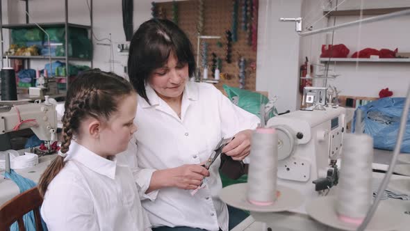 Grandma with Little Granddaughter Sew Clothes in the Factory