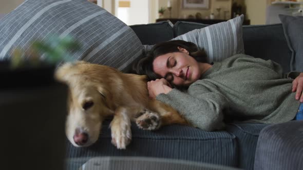 Smiling caucasian woman stroking her pet dog on sofa next to her