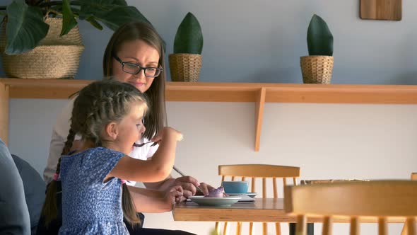 woman freelancer works while her daughter eats cake in a cafe