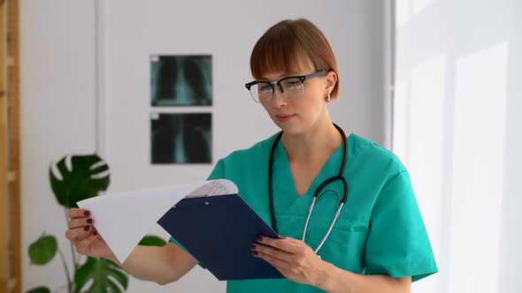 Young Woman Doctor is Looking at Report and Posing for Camera in Modern Clinic Spbas