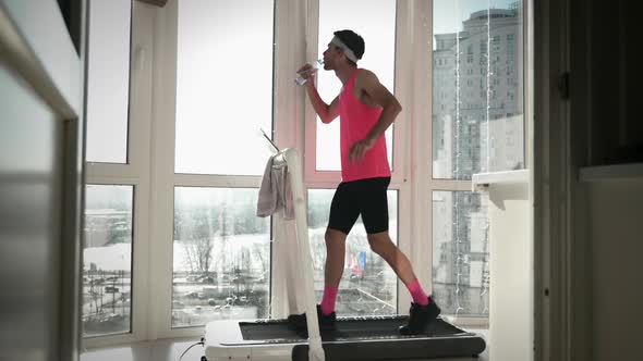 Man is drinking water during exercising on treadmill