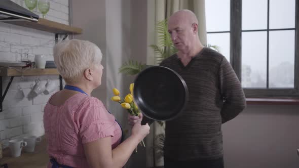 Portrait of Mature Caucasian Baldheaded Man Apologising with a Bouquet of Yellow Flowers, Angry Wife