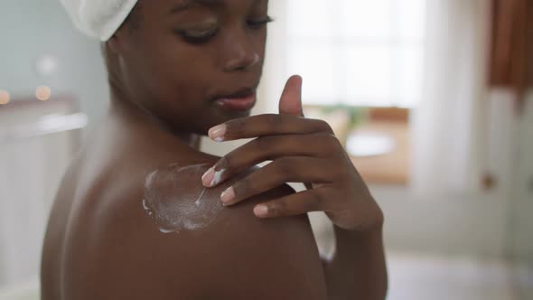 Portrait of african american attractive woman applying body balm in bathroom