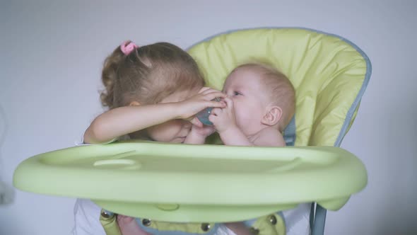 Girl Helps Brother Sitting in Soft Highchair Drink Water