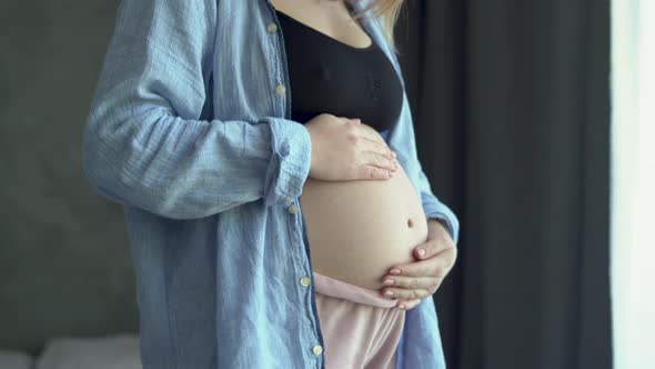 Happy Pregnant Woman Standing on Bedroom Holding and Stroking Her Big Belly at Home Close Up