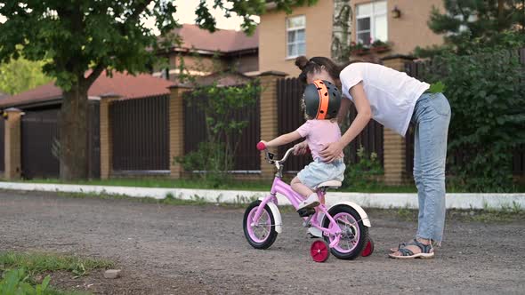 A young mother prepares her daughter for a bike ride. A girl in a safety helmet