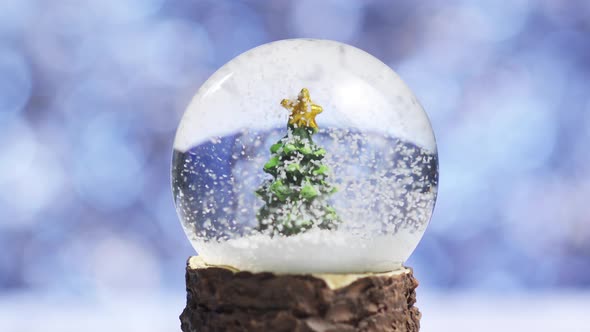 Close-up of Snowflakes Swirling Around a Christmas Tree Inside a Glass Ball