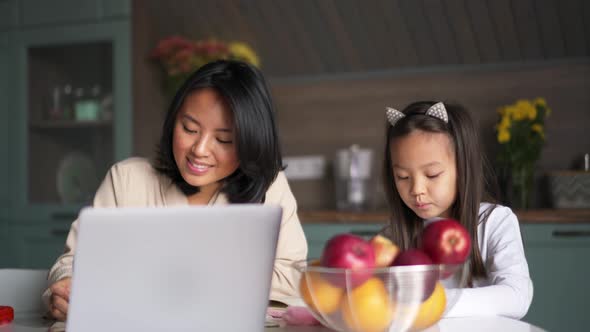 Smiling Asian mom and daughter painting in the kitchen