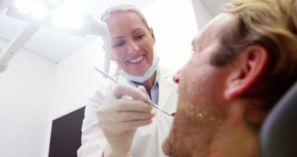 Female dentist examining male patient with dental tools