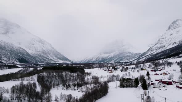 Misty mountains and snowed in village in white Manndalen valley, winter aerial