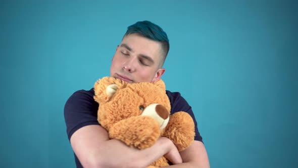 A Young Man with Blue Hair Is Holding a Teddy Bear. Alternative Man Hugs a Soft Toy on a Blue