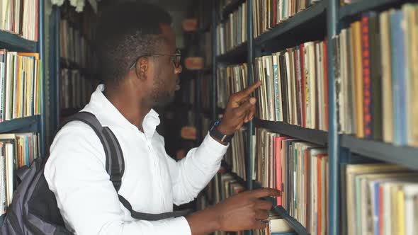 Young Male Student Choosing Book Between Shelves in the Library.